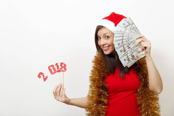 Kaunis valkoihoinen nuori onnellinen nainen punaisessa mekossa, sinisessä ja jouluhatussa, jolla on kortin numero 2018 ja valkoisella taustalla olevat setelit. Joulupukin tyttö, jolla on rahaa. Uudenvuoden loma 2018 käsite
 - Valokuva, kuva