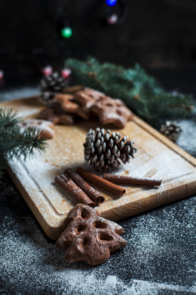 Lebkuchen für das neue Jahr und Weihnachten, Weihnachtsbaum, Zapfen, Zimt auf einem Holzschneidebrett auf dunklem Hintergrund - Foto, Bild