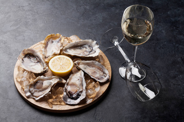 Opened oysters, ice and lemon on board and white wine on stone table - Valokuva, kuva