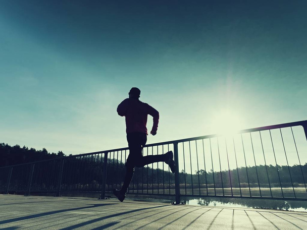 Ranní běžce v vysoké Černé legíny cvičení na mostě. Venkovní cvičení na mostě - Fotografie, Obrázek
