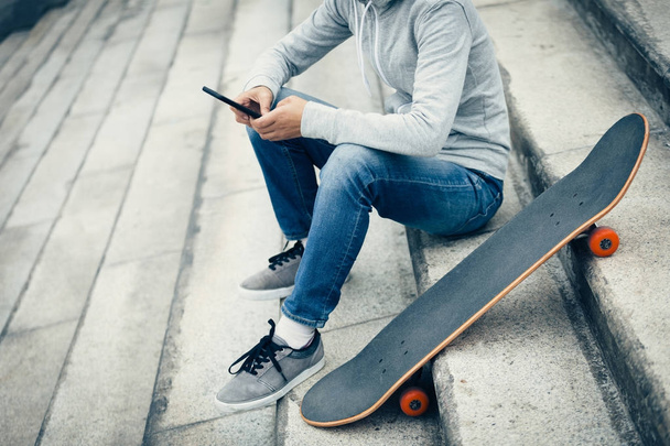 skateboarder using smartphone while sitting on city stairs with skateboard - Zdjęcie, obraz
