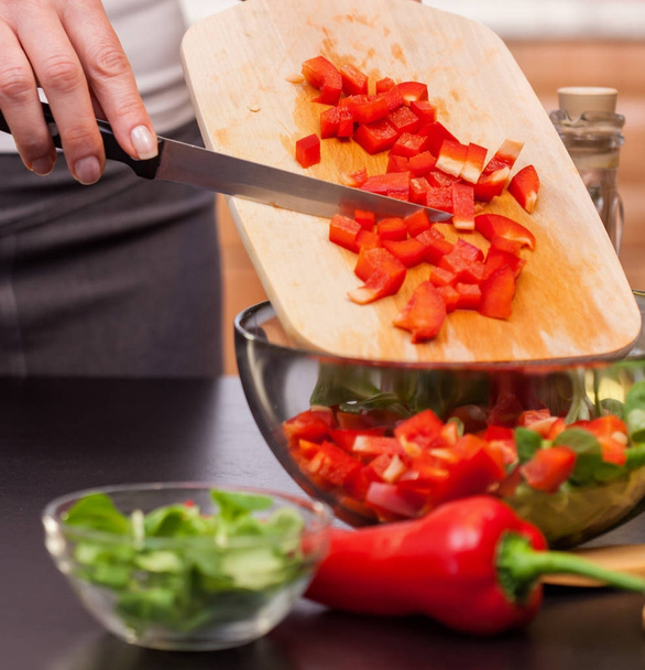Κάνοντας μια σαλάτα λαχανικών - γυναίκα κοπής κόκκινες πιπεριές βάζοντας τα κομμάτια σε ένα μπολ - Φωτογραφία, εικόνα