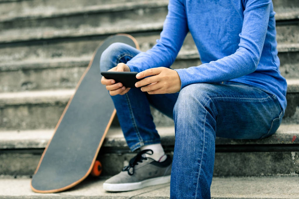 skatista usando smartphone enquanto sentado nas escadas da cidade com skate
 - Foto, Imagem