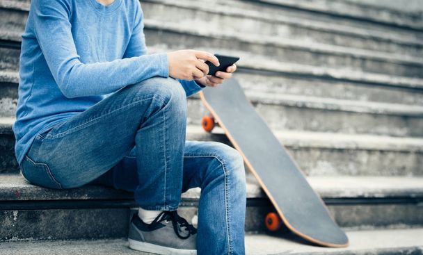 skateboarder using smartphone while sitting on city stairs with skateboard - Foto, immagini