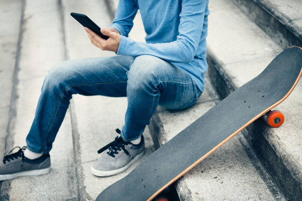 skateboarder usando smartphone mientras está sentado en las escaleras de la ciudad con monopatín
 - Foto, imagen