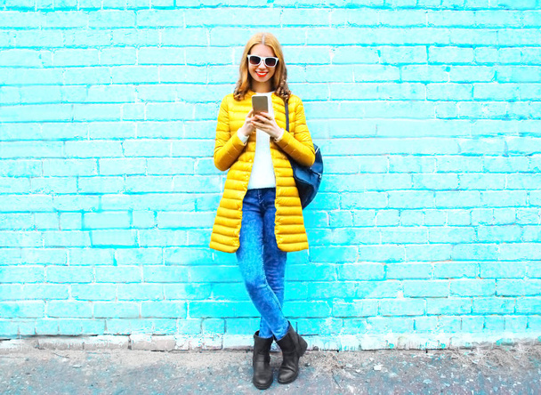 Fashion smiling woman with a smartphone on blue brick background - Фото, зображення