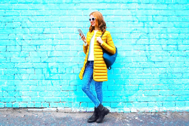Fashion young woman using smartphone on a blue brick background  - Foto, afbeelding