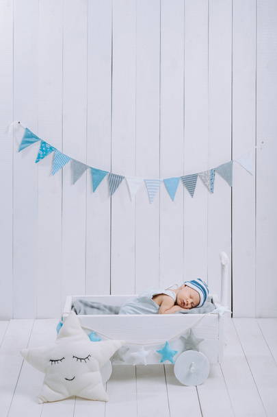 χαριτωμένο μωρό νεογέννητο στο καπέλο στον ύπνο σε ξύλινο κρεβατάκι μωρού με αστέρι μαξιλάρι γύρω από  - Φωτογραφία, εικόνα
