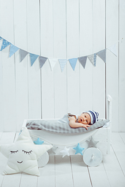 adorable infant baby in hat resting in wooden baby crib decorated with stars - Fotografie, Obrázek