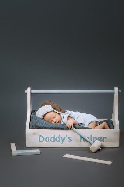 adorable baby with hammer in hand sleeping in wooden toolbox with daddys helper lettering - Photo, Image