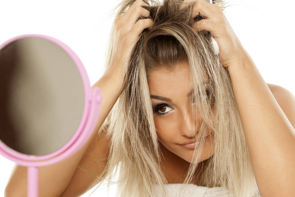 Молода красива жінка дивиться на її безладне волосся у дзеркало
 - Фото, зображення