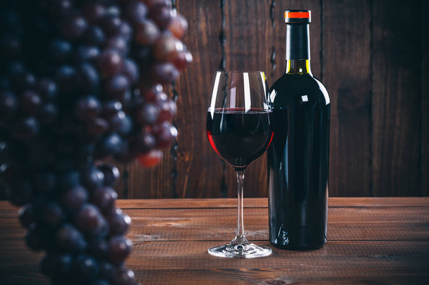Bottiglia e calice di vino rosso, uva e sughero su fondo di legno
. - Foto, immagini