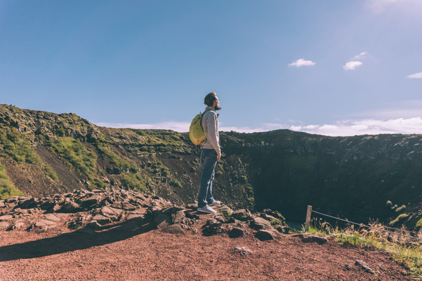 вид сбоку молодого бородатого мужчины с рюкзаком, смотрящего на живописное озеро в Исландии
 - Фото, изображение