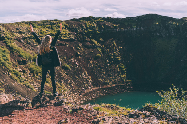 back view of girl standing with raised hands and looking at beautiful crater lake in Iceland - 写真・画像