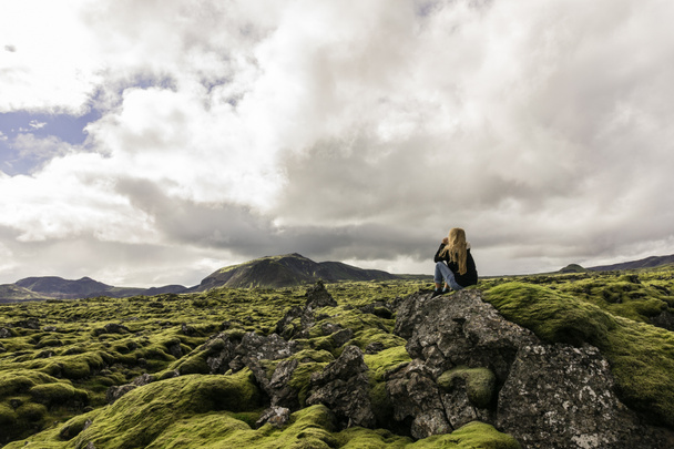 fiatal nő ül a rock és a fenséges Izlandi táj látszó - Fotó, kép