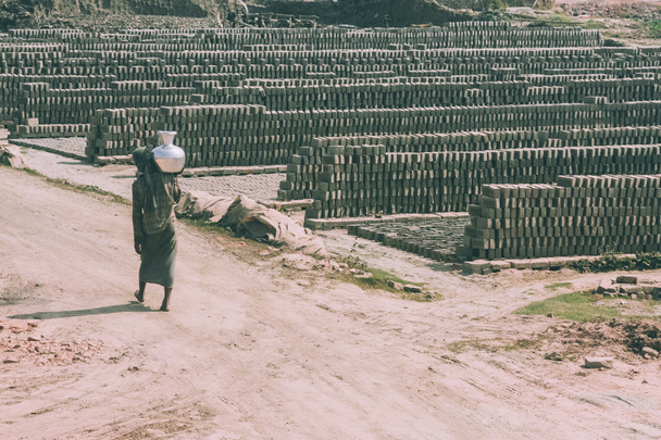 pauvre personne pieds nus portant pichet sur l'épaule et entrepôt extérieur de briques autour au Népal
 - Photo, image