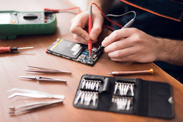 A man is repairing a mobile phone. In the frame, his hands and details of the device. - Photo, image