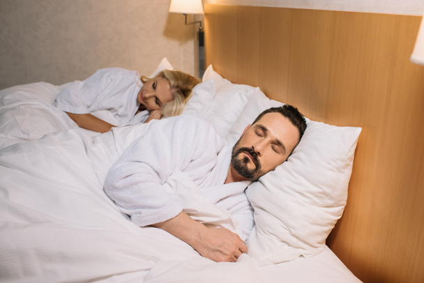 beautiful mature couple in bathrobes sleeping together in hotel room - Fotografie, Obrázek