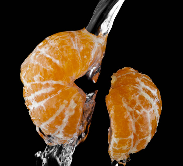 sinaasappels in dalingen van water op een zwarte achtergrond-closeup - Foto, afbeelding