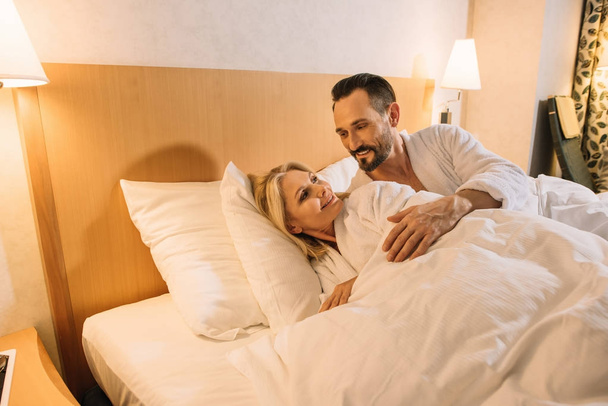 hermosa pareja de adultos en albornoces despertando en la habitación del hotel
 - Foto, imagen