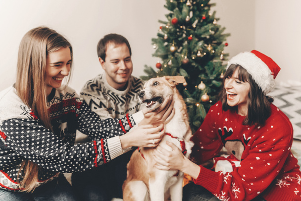 happy family in stylish sweaters and cute dog having fun near decorated Christmas tree  - Photo, Image