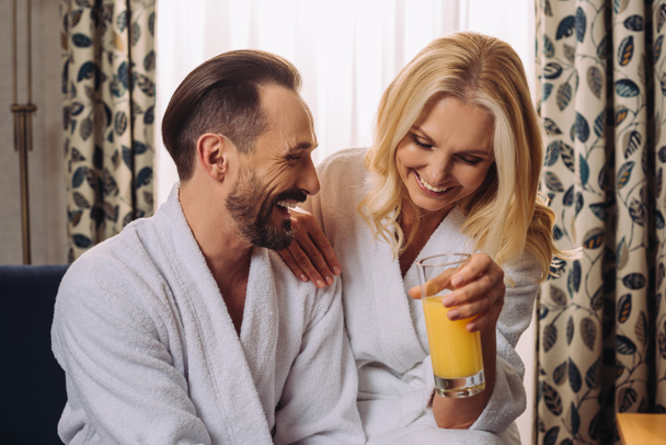 heureux couple d'âge moyen en peignoirs boire du jus pendant le petit déjeuner dans la chambre d'hôtel
 - Photo, image
