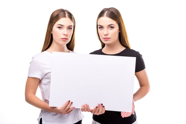 portrait of beautiful twins looking at camera while holding blank banner in hands isolated on white - Zdjęcie, obraz