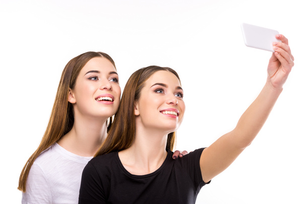retrato de gemelos sonrientes tomando selfie en el teléfono inteligente juntos aislados en blanco
 - Foto, Imagen