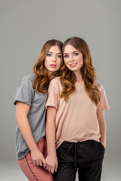 portrait of beautiful twin sisters in stylish clothing isolated on grey - Fotoğraf, Görsel