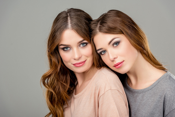 retrato de hermanas gemelas atractivas mirando a la cámara aislada en gris
 - Foto, Imagen
