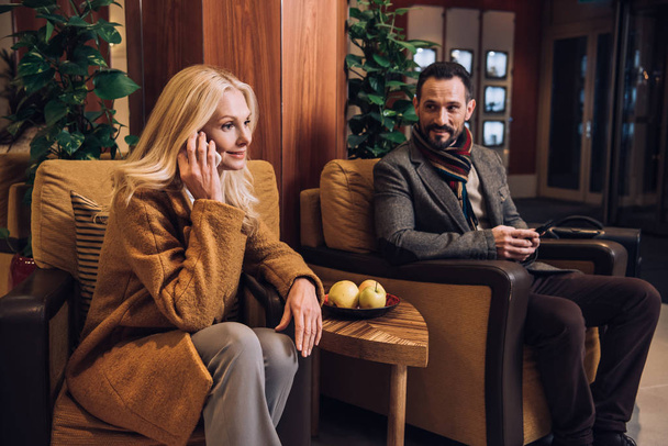 middle aged couple using smartphones while sitting and waiting in hotel hallway - Valokuva, kuva