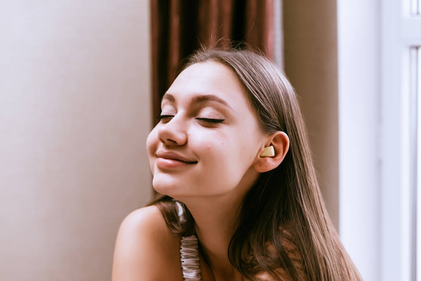 a smiling young girl enjoys the silence, in the ears earplugs against the noise - Foto, Imagen