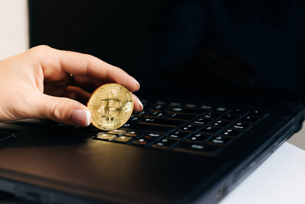 girl financier working on a laptop, holding in her hand a valuable gold bitcoin - Foto, imagen