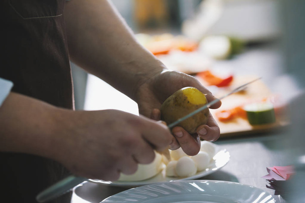 Chef is peeling potatoes for salad with knife in commercial kitchen - Foto, Imagen