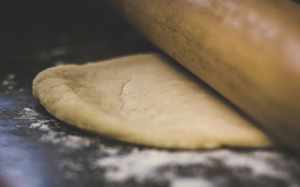 Making fresh homemade dough. The dough is being rolled out on the counter top with a rolling pin. Flour has been sprinkled on the table and though dough.  - Foto, Imagen