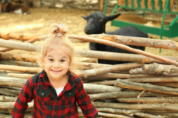 Cute little girl near enclosure with goats on farm - Фото, зображення