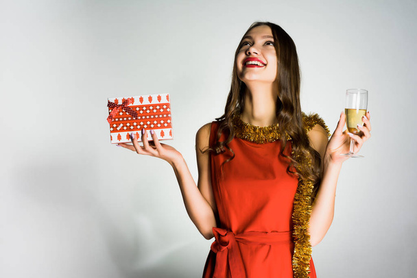 ein fröhlich lachendes Mädchen im roten Kleid feiert das neue Jahr 2018, erhält ein Geschenk vom Weihnachtsmann, hält ein Glas Champagner in der Hand - Foto, Bild