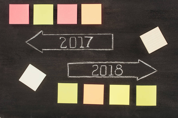 top view of arranged empty sticky notes and arrows with 2017, 2018 year signs on dark wooden surface - Foto, Bild