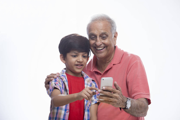 Isoisä ja pojanpoika käyttävät älypuhelinta
 - Valokuva, kuva