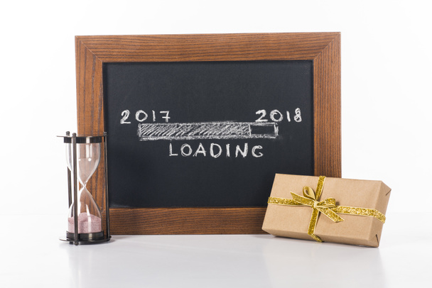 vista de cerca de pizarra con 2017 a 2018 letras de carga con reloj de arena y regalo cerca de aislado en blanco
 - Foto, Imagen