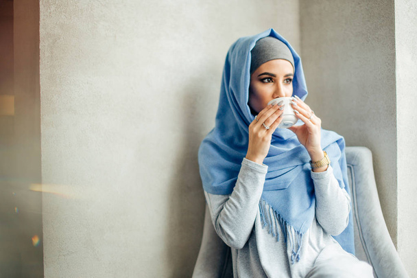 Csinos, fiatal muszlim nő, egy csésze kávé vagy tea akcióban - Fotó, kép