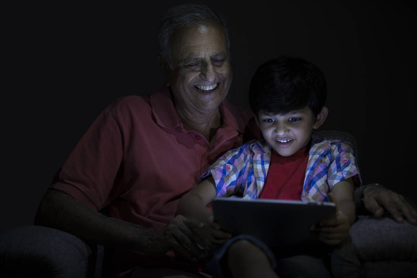 Дедушка и внук используют цифровые планшеты в темной комнате
 - Фото, изображение