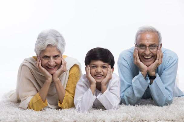 Grand-parents et petit-fils couchés sur le tapis avec la main sur le menton
 - Photo, image