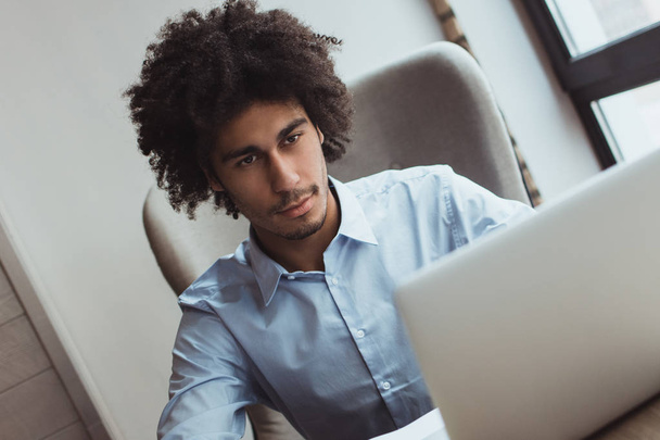 Homem de negócios moderno. Bonito jovem empresário olhando para seu laptop enquanto sentado em sua mesa de escritório
 - Foto, Imagem
