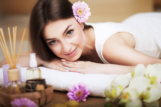Portrait of a beautiful girl in a spa. Gentle look. Flowers in hair. Aroma oil. Massage cabinet. The concept of health and beauty. - Photo, Image