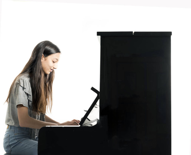 teenage brunette girl and black upright piano in studio - Fotó, kép