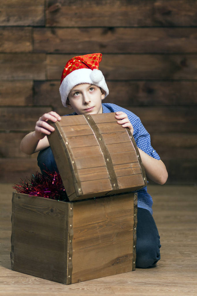 Valkoihoinen teini katsoo ylös huomaavaisesti, kun hän avaa puisen arkun joulukoristeilla. Pystykuva
. - Valokuva, kuva