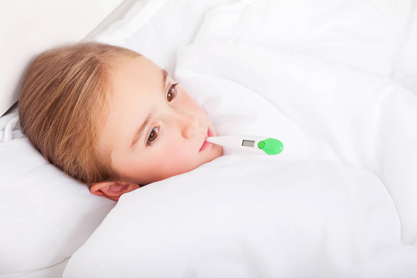 Sick girl lying in bed with a thermometer in mouth - Фото, изображение