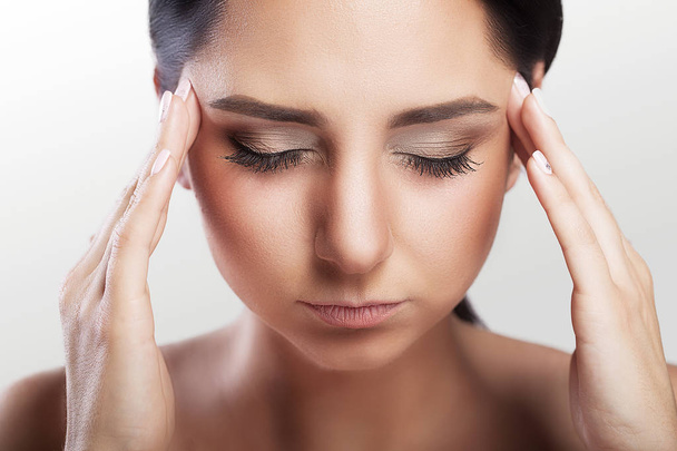 Headache, migraine and stress. A woman worries about a woman who suffers from headaches. On a gray background. Holds his hands to his forehead. Professional makeup. Health protection. - Photo, image