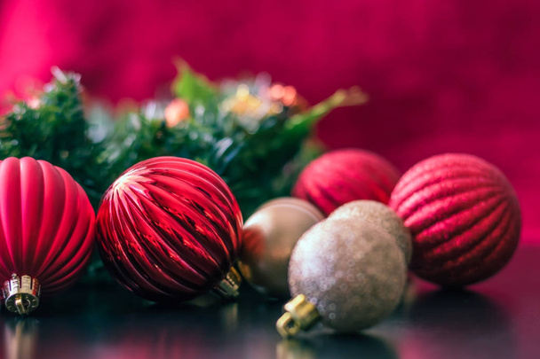 Los adornos de bolas de Navidad rojos y dorados se fotografian desde un ángulo lateral mientras están sentados en una superficie de mesa negra brillante esperando a ser colgados en el árbol de Navidad.
. - Foto, imagen
